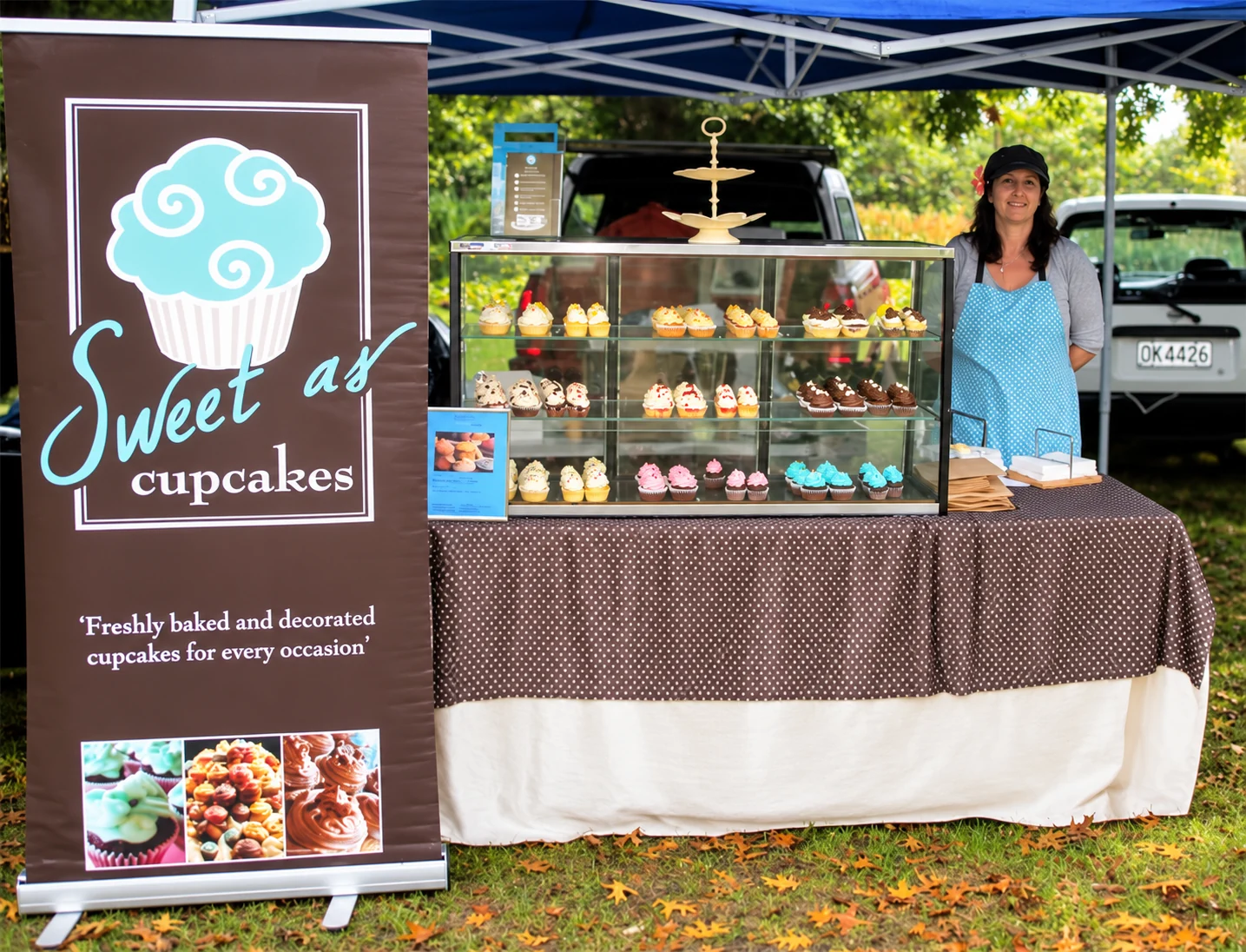 The lady behind the Sweet As Cupcakes counter at a market stall, with a display of decorated cupcakes